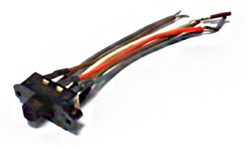 O objeto é uma pequena chave de reversão/seletora elétrica, provavelmente para painéis ou comandos de máquinas. É uma peça preta e retangular, com terminais na parte de trás conectados a vários fios coloridos (alguns brancos/cinzas, um vermelho/laranja) para ligação em um circuito elétrico. Ela serve para selecionar a direção (frente/trás, por exemplo) ou alternar entre dois circuitos.