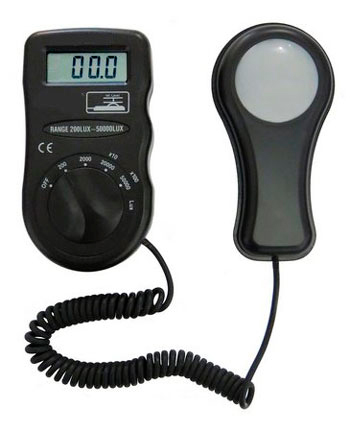 Esta é a foto de um luxímetro, um instrumento usado para medir a intensidade da luz. Consiste em duas partes pretas conectadas por um fio enrolado: Um corpo principal retangular com um display digital mostrando "00.0" e um seletor giratório de alcance de medição (de 200 a 50.000 lux). Um sensor de luz em forma de sonda, com uma cúpula branca na ponta, que é colocado onde a luz será medida. O aparelho é preto e compacto.